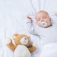 Baby Junge mit Schnuller im Mund schlafen mit Teddybär auf dem Bett