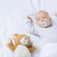 Baby Junge mit Schnuller im Mund schlafen mit Teddybär auf dem Bett