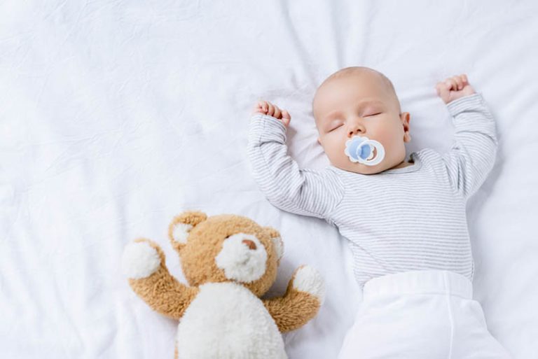 Baby Junge mit Schnuller im Mund schlafen mit Teddybär auf dem Bett