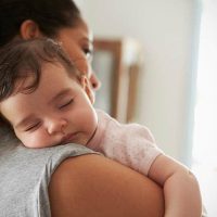 Mutter trägt schlafendes Baby auf der Schulter