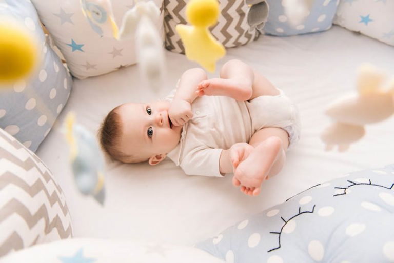 niedlichen Baby-Jungen in der Krippe liegen und beobachten die Spielzeuge