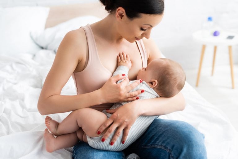 junge attraktive Mutter, die ihr Baby auf dem Bett stillt