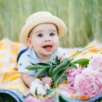 süßes Baby, das Hut trägt und auf Bauch mit Blumen im Freien liegt