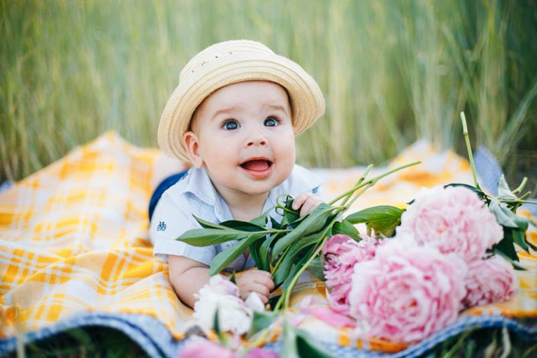 süßes Baby, das Hut trägt und auf Bauch mit Blumen im Freien liegt