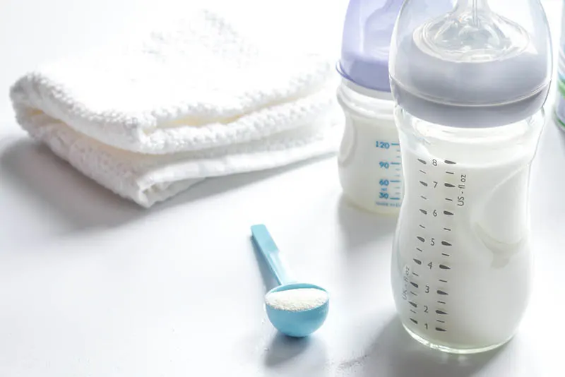 ein Schwamm mit Babynahrung und zwei Flaschen Milch und ein weißes Handtuch auf dem Tisch