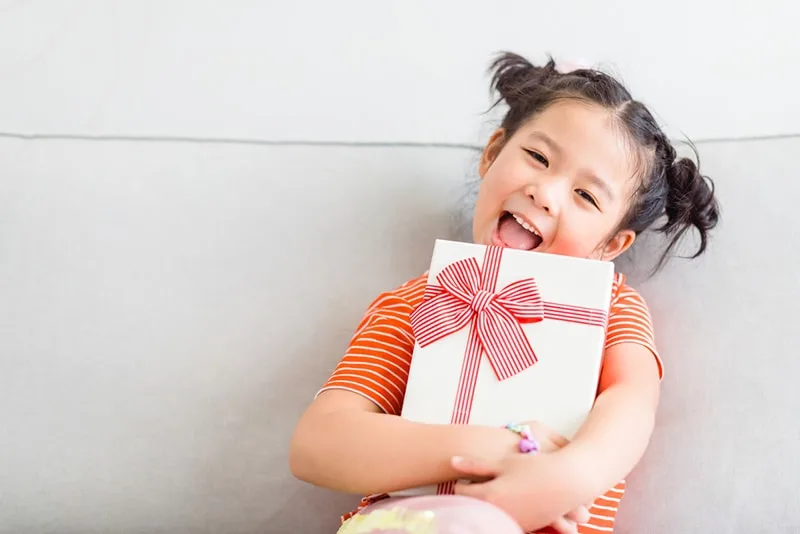 ein süßes kleines Mädchen, das lächelt und ein Geschenk mit beiden Händen hält