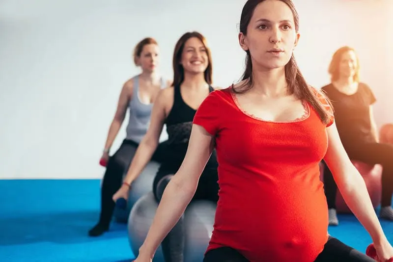 eine Gruppe schwangerer Frauen, die auf Pilatesball sitzen und Gewichte heben