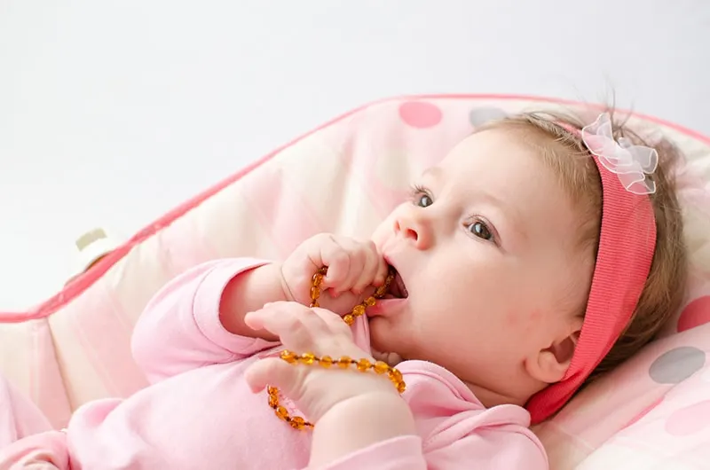 entzückendes Baby in rosa Kleidern, die bernsteinfarbene Kinderkrankheiten kauen