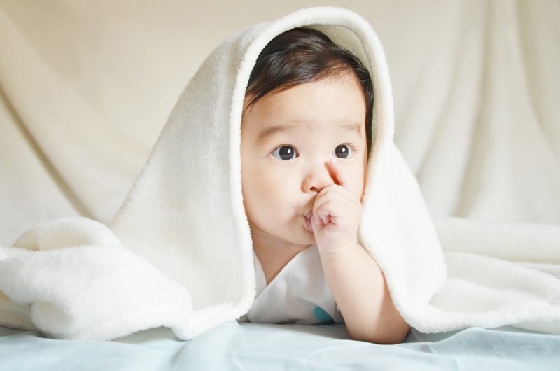entzückendes Baby liegend bedeckt Decke mit Decke und saugendem Finger