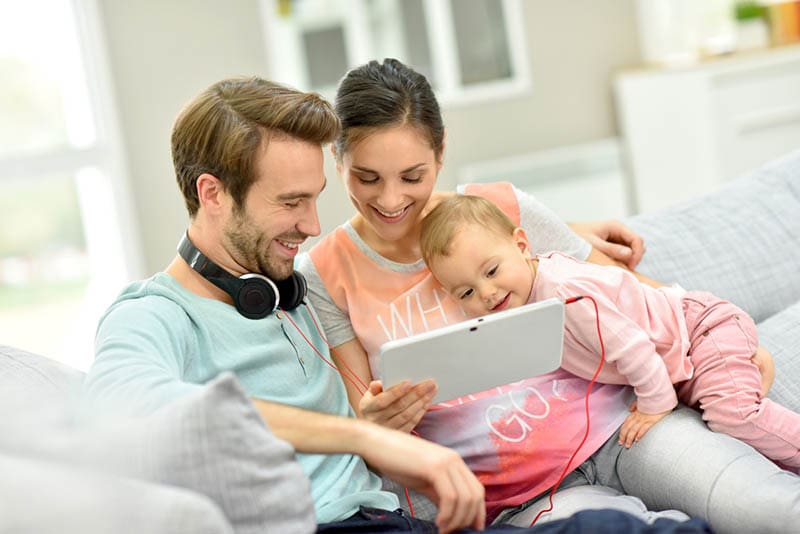glückliche Eltern, die mit ihrem Baby auf der Couch sitzen und Musik hören