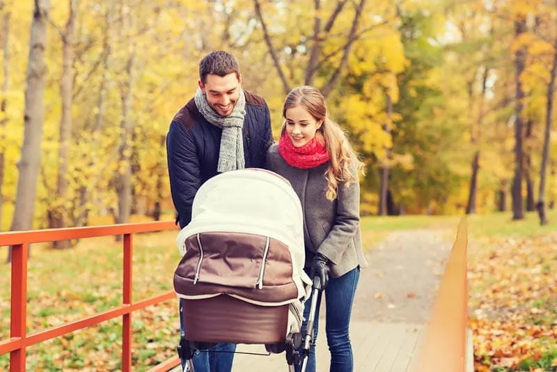 glückliche Eltern spazieren im Wald mit Baby im Kinderwagen