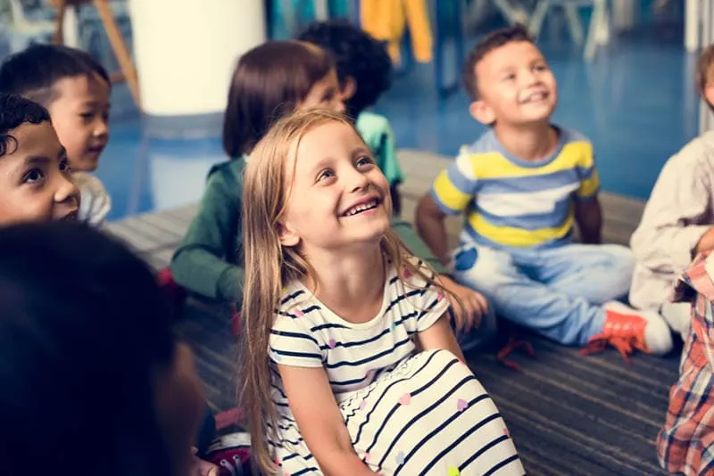glückliche Gruppe von Kindern, die auf dem Boden in der Kindertagesstätte sitzen