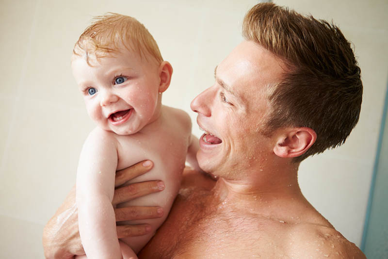 glücklicher Vater duschend zusammen mit lächelndem Baby 