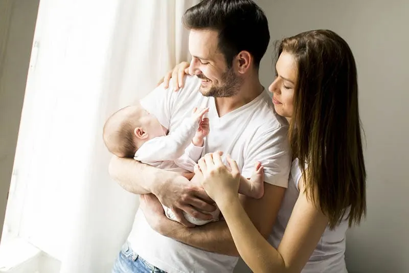 glücklicher Vater hält neugeborenes Baby mit Frau am Fenster