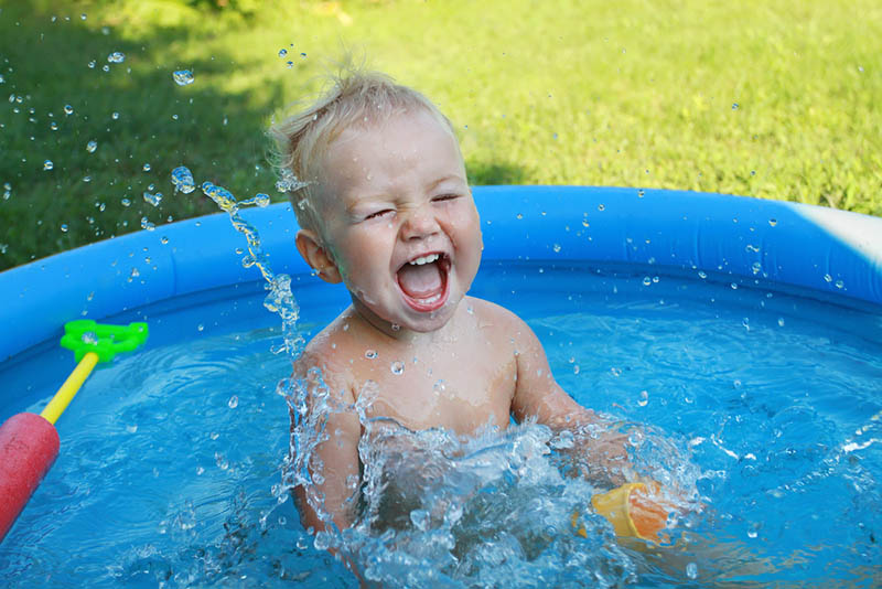 glückliches Baby spielt im Pool und lacht am sonnigen Tag