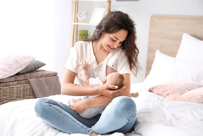 glückliches Mutter stillendes Baby beim Sitzen auf dem Bett