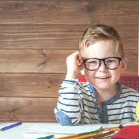 süßer Junge mit Brille, der am ersten Schultag am Tisch in der Klasse sitzt