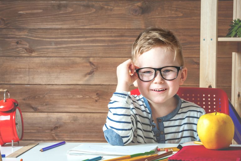 süßer Junge mit Brille, der am ersten Schultag am Tisch in der Klasse sitzt