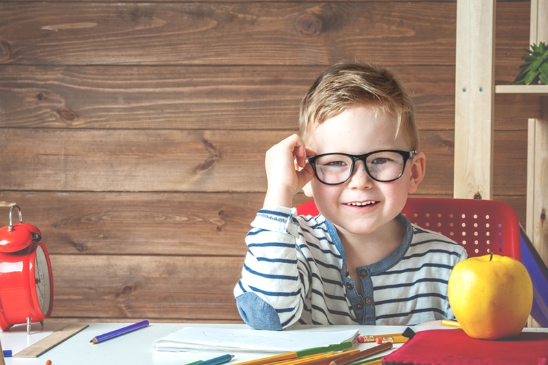 süßer Junge mit Brille, der am ersten Schultag am Tisch in der Klasse sitzt