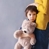 trauriger kleiner Junge, der Teddybär hält und seine Mutter umarmt