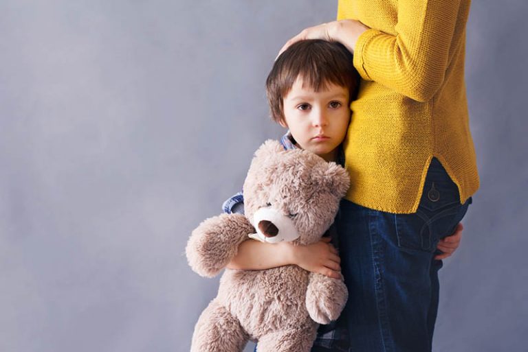 trauriger kleiner Junge, der Teddybär hält und seine Mutter umarmt