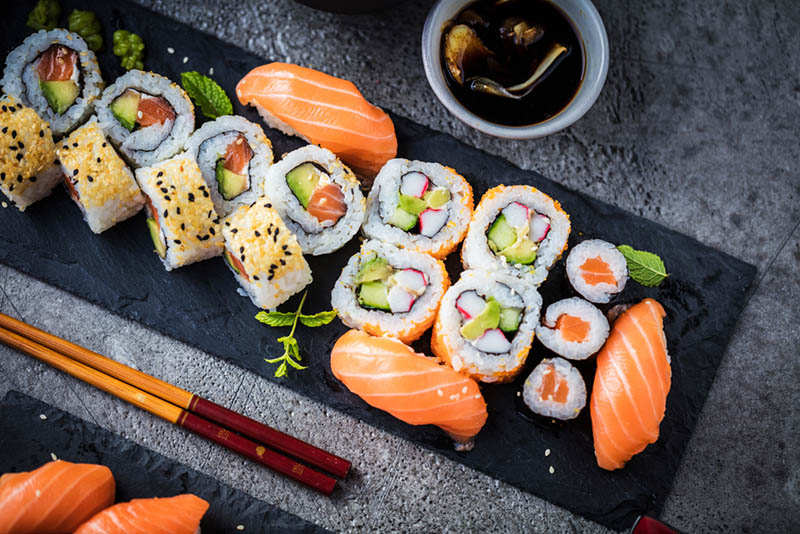 japanische Sushi-Rollen mit Thunfisch, Lachs, Garnelen, Krabben und Avocado, serviert auf schwarzem Teller