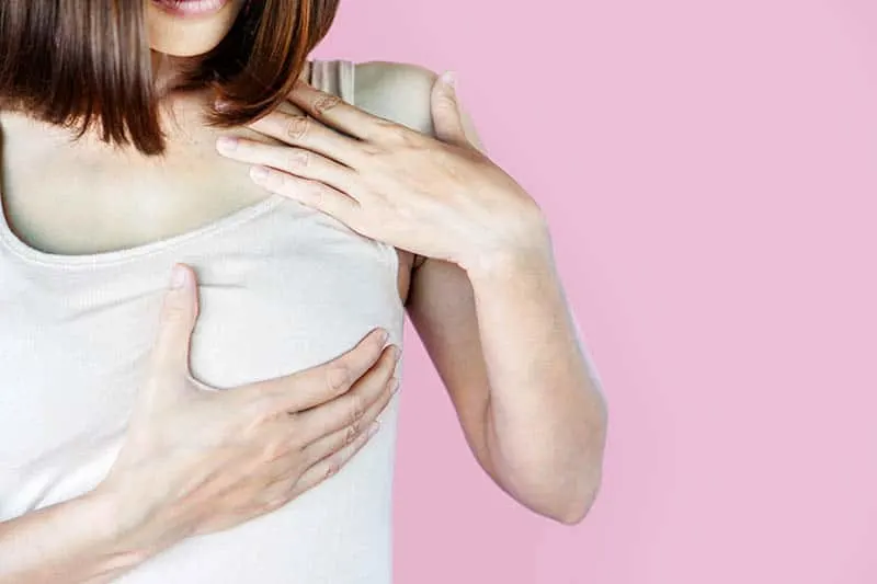 junge Frau im weißen Hemd, das ihre Brüste wegen des Schmerzes der schmerzenden Brustwarzen hält