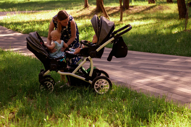junge Frau sitzt Babys in einem Zwillingskinderwagen im Park