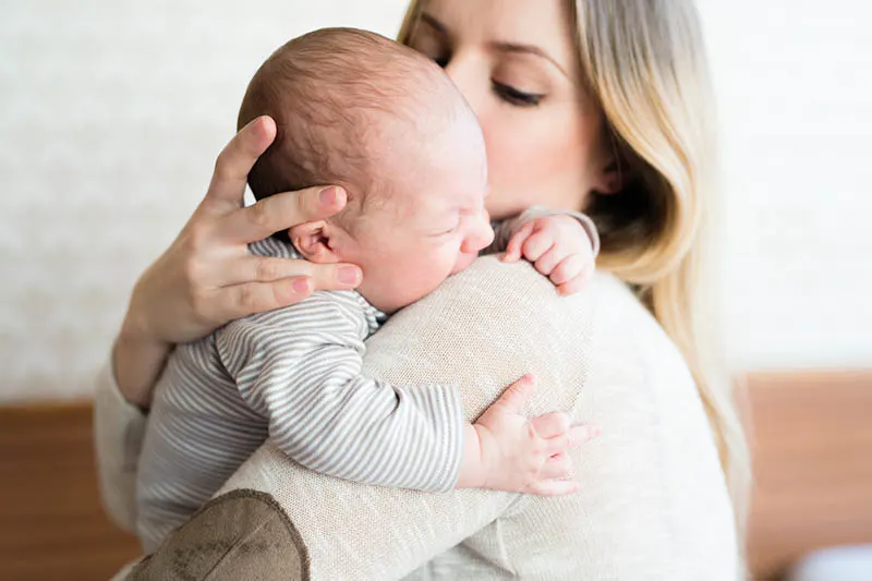 junge Mutter hält weinendes Baby auf ihrer Schulter