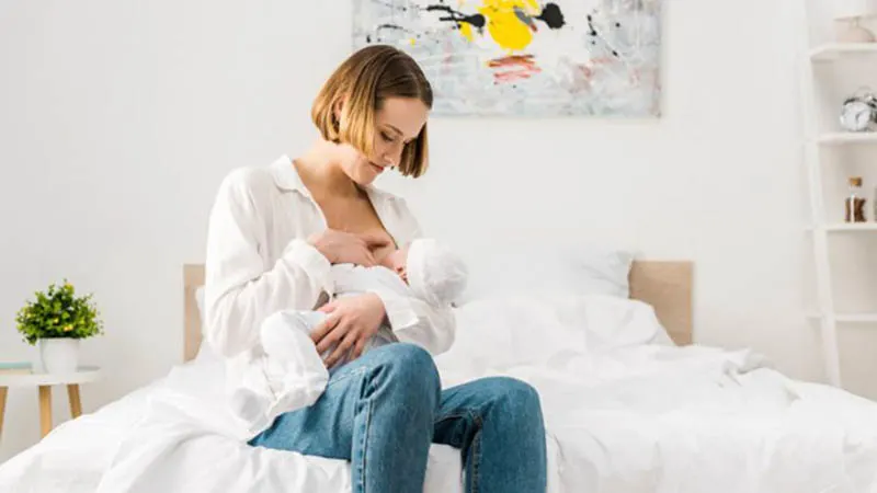 junge Mutter stillt Baby auf dem Bett während der Brustkompression