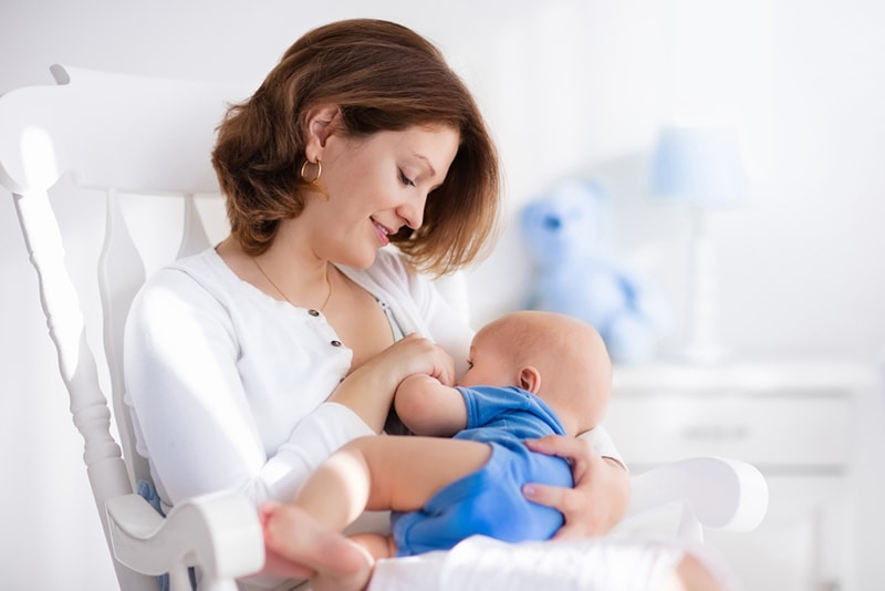 junge Mutter stillt ihr Baby auf weißem Pflegestuhl