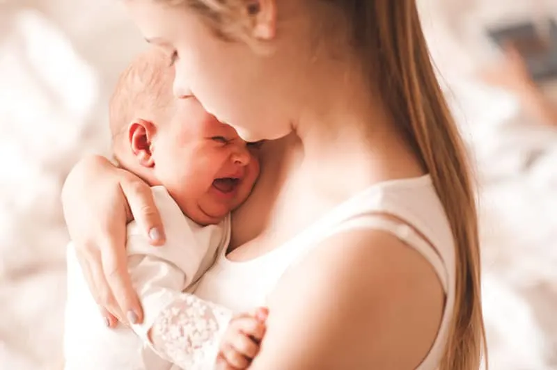 junge Mutter tröstet weinendes Baby auf ihrer Brust