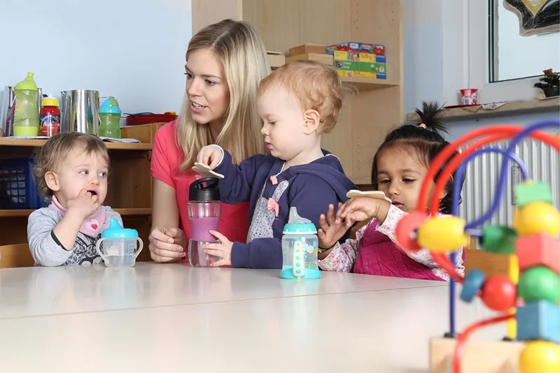 junger Lehrer, der Babys beim Spielen und Trinken der Wasserflasche beobachtet