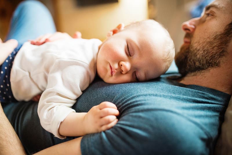 junger Vater hält schlafendes Baby auf seinem Bauch