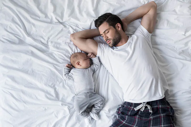 junger Vater schläft mit niedlichen neugeborenen Baby in weißen Laken