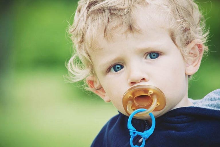süßes Baby mit lockigem Haar, das Gummischnuller saugt