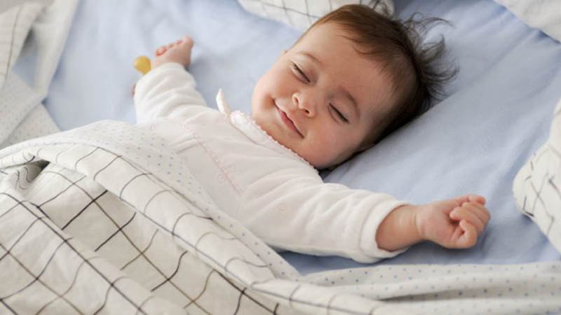 kleiner Junge auf dem Bett liegend mit ausgebreiteten Armen und lachend