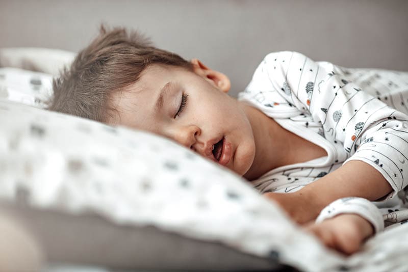 kleiner Junge schlafend im Bett in Pijama mit offenem Mund