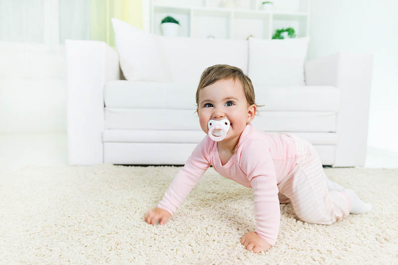 lächelnd Baby Mädchen saugen Schnuller und krabbeln auf dem Boden im Wohnzimmer