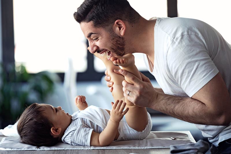 lächelnd jungen Vater tun Gymnastik mit Baby auf dem Wickeltisch