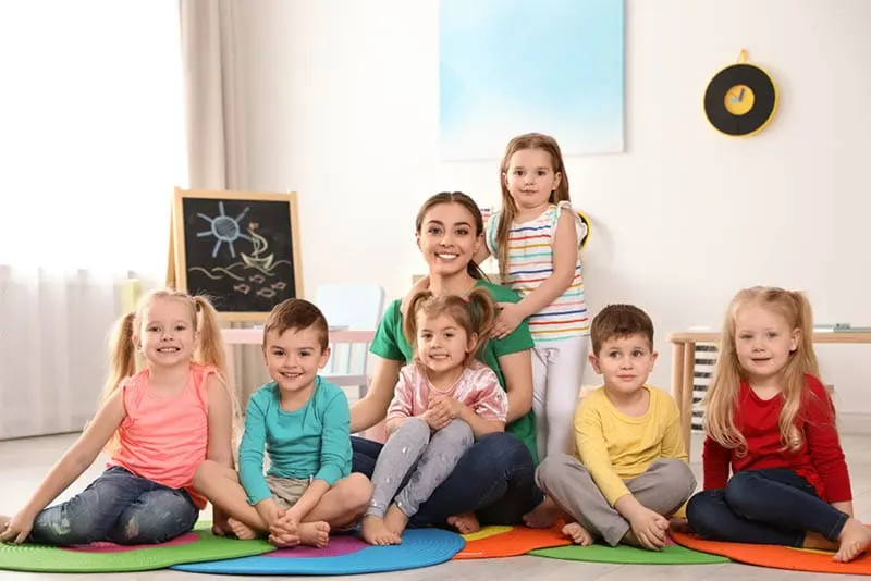 lächelnder Lehrer mit glücklichen Kindern, die auf dem Boden sitzen und posieren