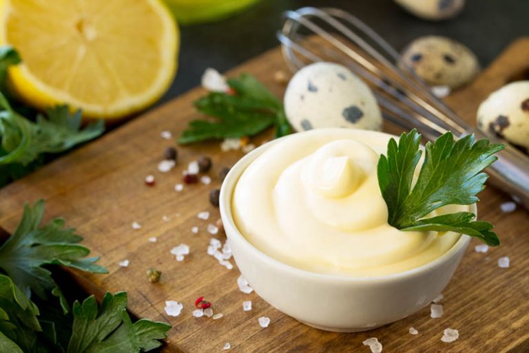 Schale mit leckerer Mayonnaise und kleinen Eiern und Gewürzen auf dem Holztisch