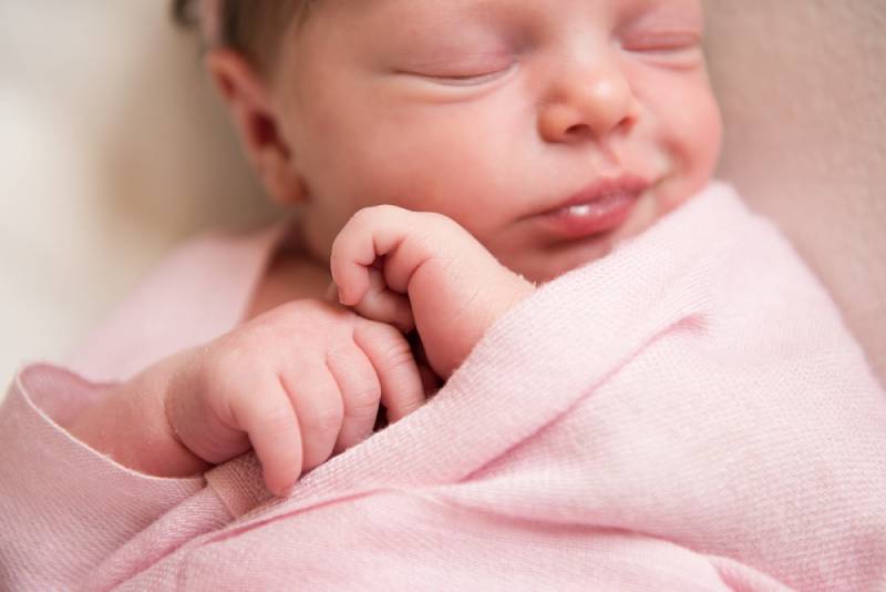 neugeborenes Baby Mädchen eingewickelt in rosa Decke lachend im Schlaf