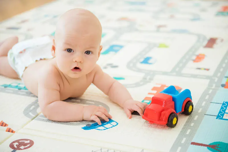 niedlich fett Baby in Windeln liegen auf der Spielmatte mit Auto Spielzeug