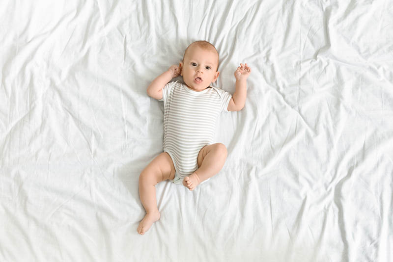 niedlichen Baby Junge auf dem weißen Blatt auf dem Bett liegen