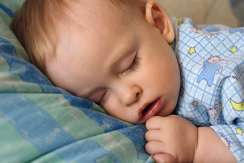 niedlichen Baby-Junge in Pijama schlafen auf dem Bauch mit offenem Mund