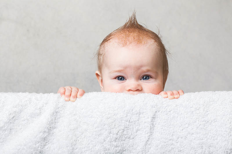 niedlichen Baby Junge mit lustigen Frisur versteckt hinter dem Handtuch