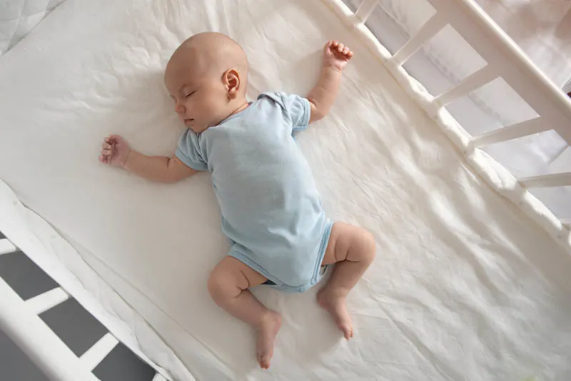 niedlichen Baby Junge schlafen in der Krippe auf weißem Blatt
