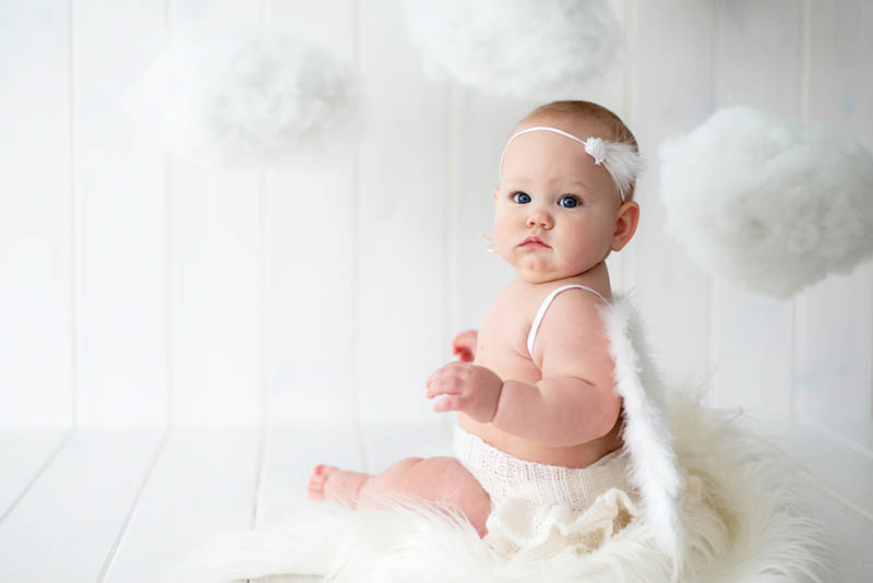 niedlichen Baby-Mädchen trägt Engelsflügel und posiert für Fotoshooting auf dem Boden