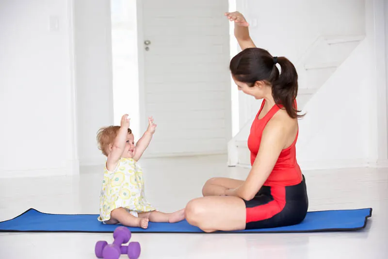 niedlichen Baby Mädchen tun Yoga mit ihrer Mutter auf dem Boden